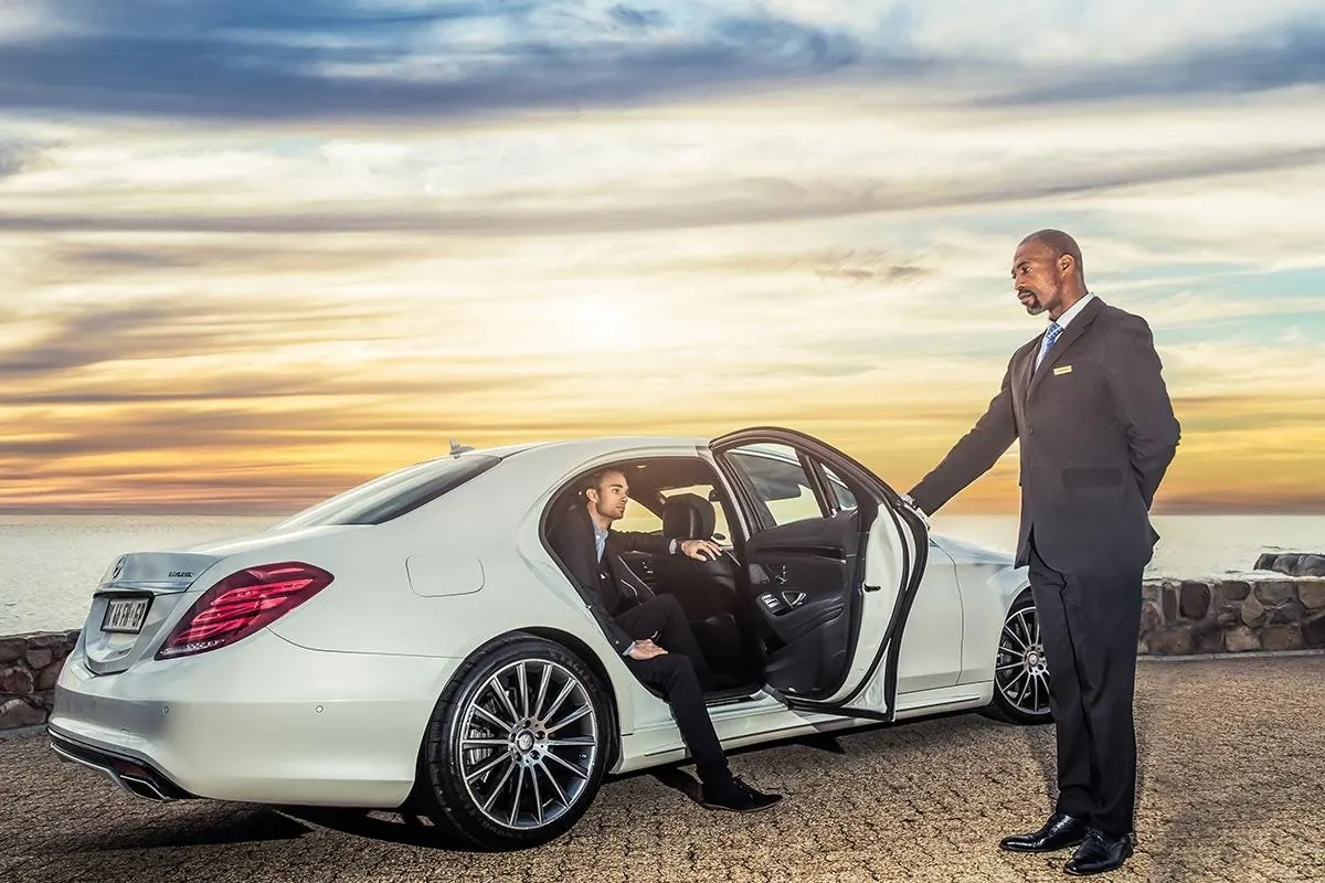 Chauffeur opening a white Mercedes S-Class at sunset